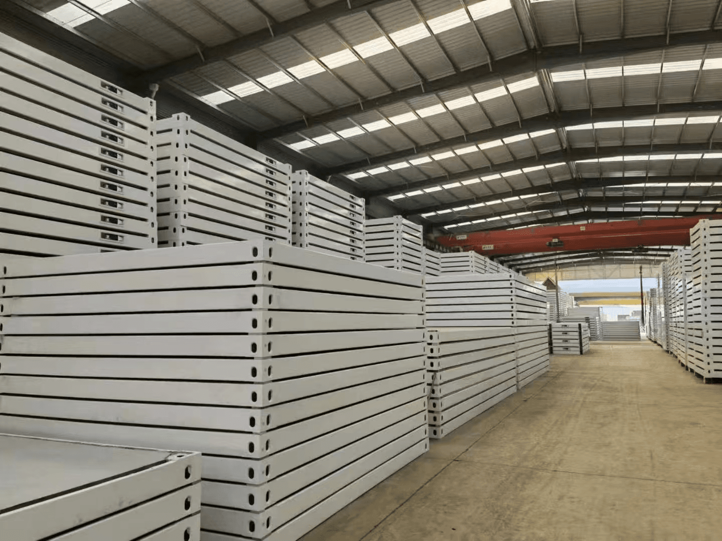 Stacked insulated sandwich panels staged under a red overhead crane