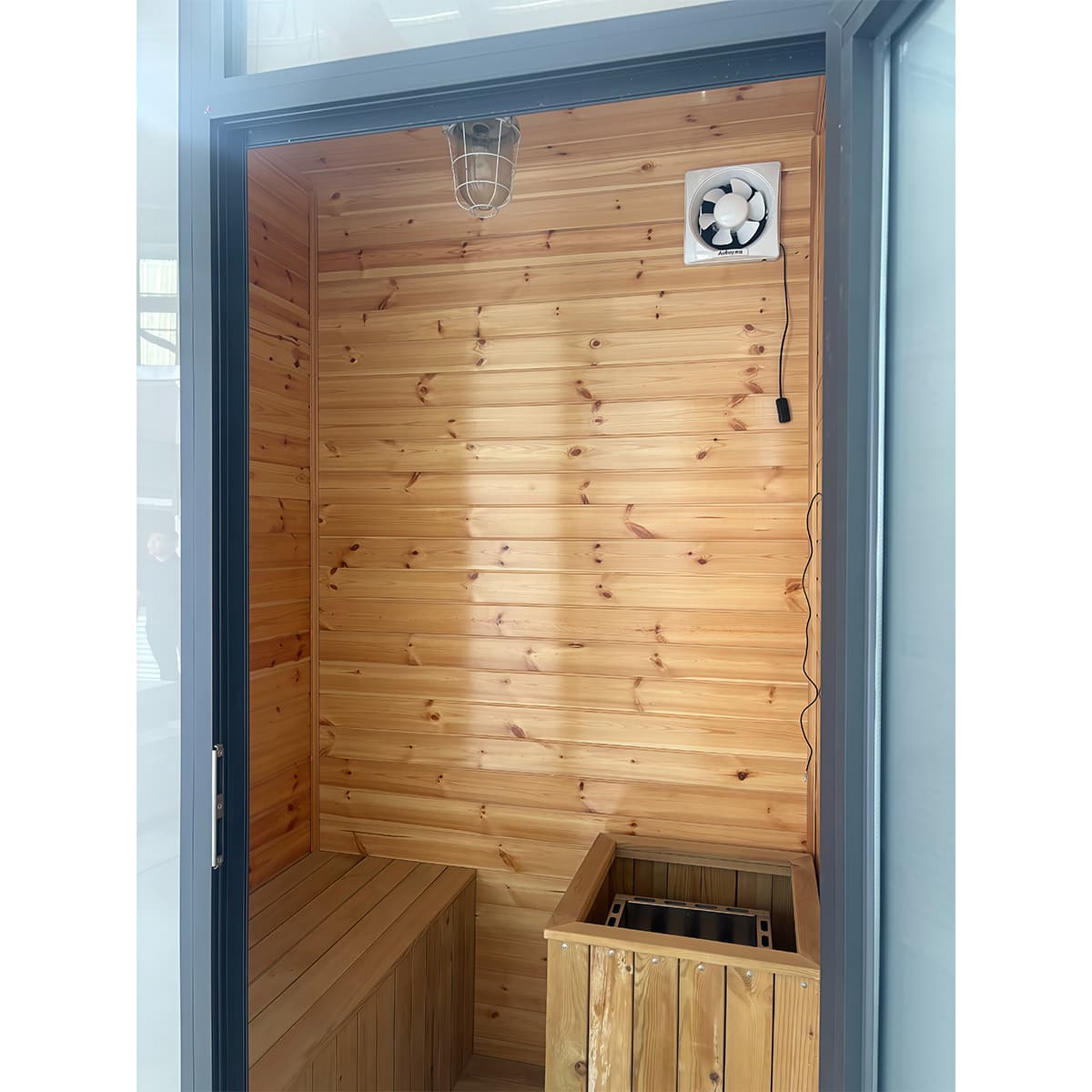 Timber-lined sauna cabin interior with bench seating, heater bay, and ventilation fan